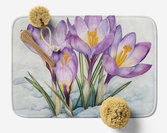 Può includere: Un dipinto ad acquerello di crochi viola con centri gialli, su uno sfondo blu chiaro. I fiori sono disposti in un gruppo, con i loro steli e foglie visibili. Il dipinto è incorniciato da un bordo bianco.