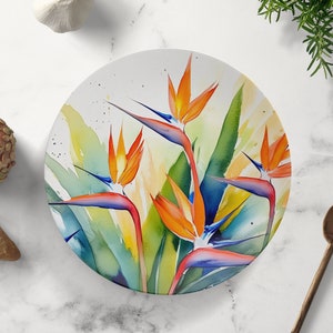 Pu&ograve; includere: Un piatto rotondo in ceramica con un design ad acquerello di fiori di uccello del paradiso arancioni, blu e verdi.
