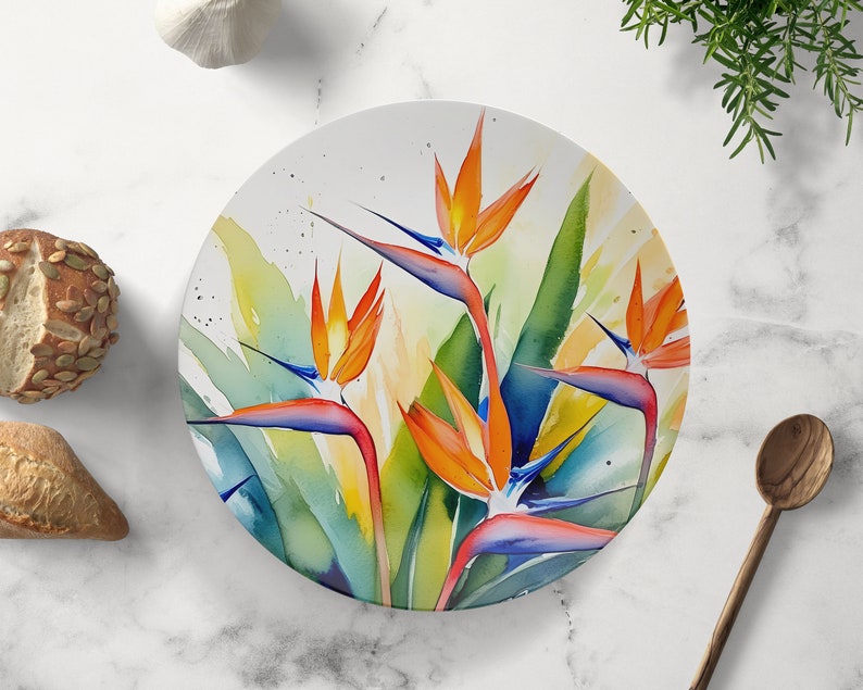 Pu&ograve; includere: Un piatto rotondo in ceramica con un design ad acquerello di fiori di uccello del paradiso arancioni, blu e verdi.
