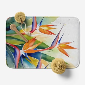 May include: A bath mat with a watercolor design of orange, blue, and green bird of paradise flowers. The mat is white with a textured surface.