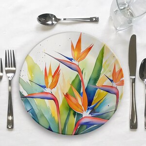 Pu&ograve; includere: Un piatto da cena in ceramica bianca con un design ad acquerello colorato di fiori di uccello del paradiso. Il piatto presenta una miscela vibrante di tonalit&agrave; arancio, giallo, blu e verde.