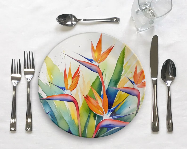 Pu&ograve; includere: Un piatto da cena in ceramica bianca con un design ad acquerello colorato di fiori di uccello del paradiso. Il piatto presenta una miscela vibrante di tonalit&agrave; arancio, giallo, blu e verde.