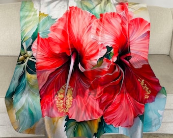 Può includere: Una morbida coperta con un vivace design ad acquerello di un grande fiore di ibisco rosso con stami gialli. La coperta mostra anche foglie verdi e uno sfondo azzurro, creando un tema tropicale.