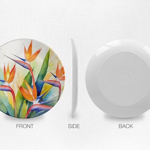 Pu&ograve; includere: Un piatto in ceramica bianca con un design ad acquerello colorato di fiori di uccello del paradiso arancioni, blu e verdi.