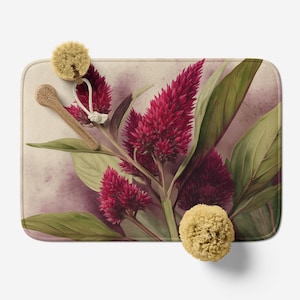 May include: A rectangular bath mat featuring a watercolor design of vibrant red celosia flowers and green leaves. A wooden spoon and two natural sponges are placed on the mat. The background has a soft, watercolor-like effect with shades of pink and purple.