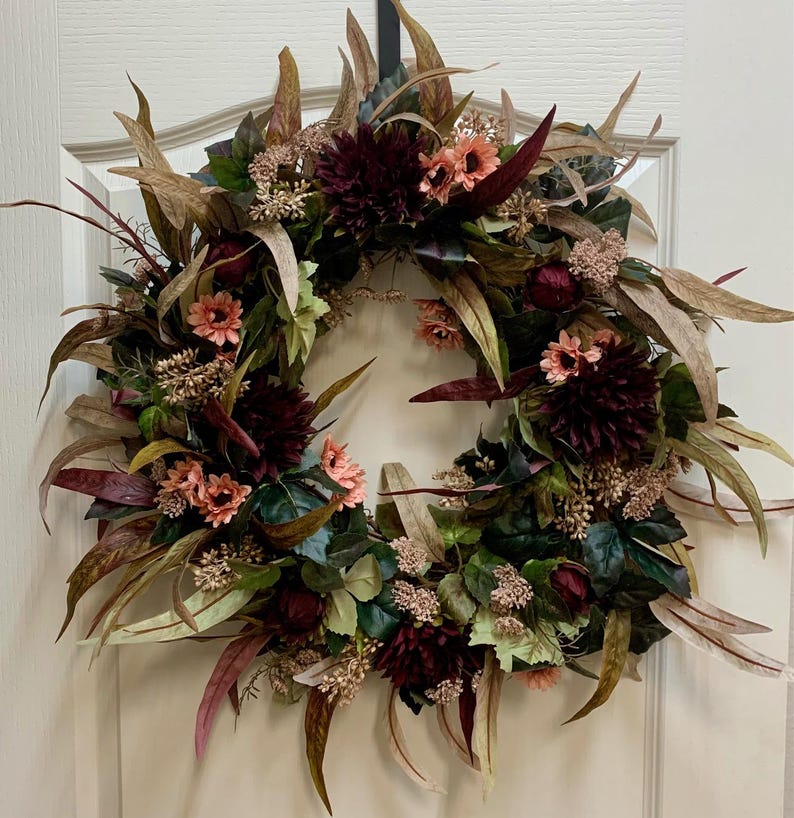Pode incluir: Uma coroa de flores bord&ocirc; e rosa com folhas de eucalipto e detalhes de bagas. A coroa &eacute; feita com flores e folhagem artificiais.