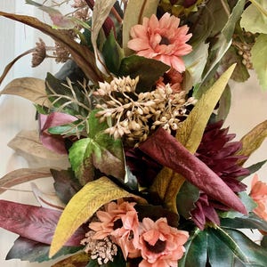 Pode incluir: Uma coroa de outono com folhas de cor bord&ocirc;, verde e marrom, juntamente com flores cor-de-rosa.