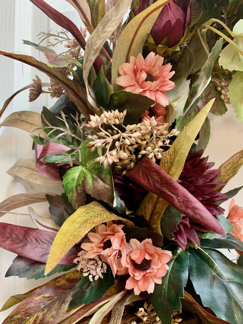 Pode incluir: Uma coroa de outono com folhas de cor bord&ocirc;, verde e marrom, juntamente com flores cor-de-rosa.