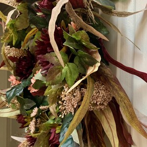 Pode incluir: Uma coroa de outono com flores bord&ocirc;, rosa e verde, folhas marrons e verdes e caules bege.