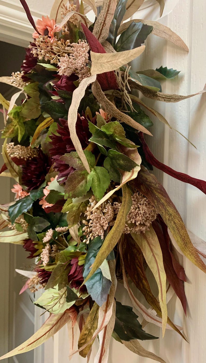 Pode incluir: Uma coroa de outono com flores bord&ocirc;, rosa e verde, folhas marrons e verdes e caules bege.