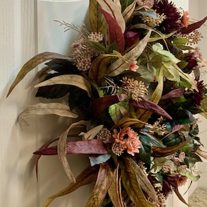 Pode incluir: Uma coroa de outono com folhas e flores de cor bord&ocirc;, p&ecirc;ssego e marrom. A coroa &eacute; feita de materiais artificiais e &eacute; perfeita para decorar uma porta ou parede.
