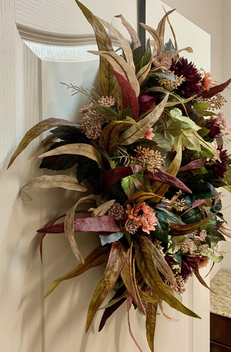 Pode incluir: Uma coroa de outono com folhas e flores de cor bord&ocirc;, p&ecirc;ssego e marrom. A coroa &eacute; feita de materiais artificiais e &eacute; perfeita para decorar uma porta ou parede.