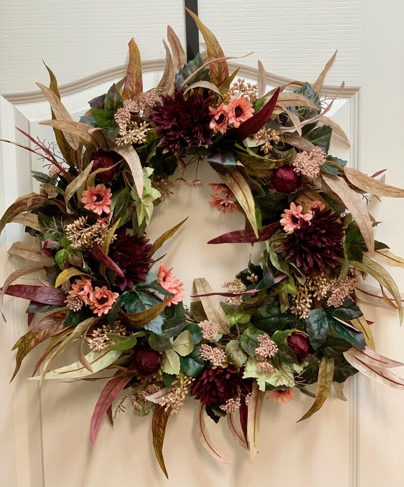 Pode incluir: Uma coroa de flores de cor bord&ocirc; e p&ecirc;ssego com folhas de eucalipto e vegeta&ccedil;&atilde;o. A coroa &eacute; feita de flores artificiais e &eacute; perfeita para a decora&ccedil;&atilde;o de outono.
