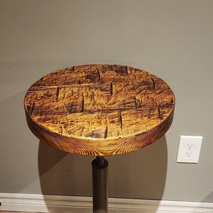May include: A round wooden table with a distressed finish and a black metal base with four legs. The table is on a braided rug.