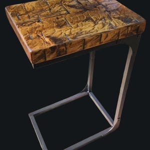 May include: A wooden side table with a rectangular top and a metal frame. The tabletop has a textured, mosaic-like pattern in shades of brown and tan. The metal frame is a silver color and has a C-shape design.