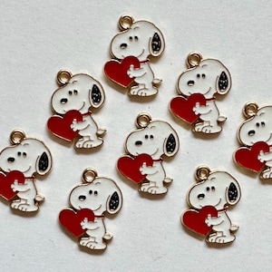 May include: Ten gold-toned metal charms, each featuring a white enamel Snoopy character holding a bright red heart. Each charm includes a small circular loop at the top for attachment, showcasing a consistent design of the cartoon dog.