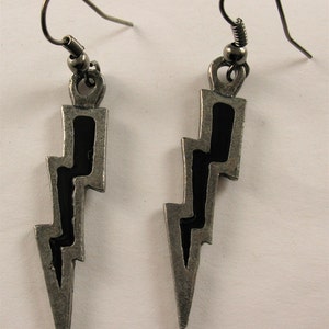 May include: A pair of silver-toned earrings in the shape of lightning bolts. Each earring has a black enamel inlay and a hook for pierced ears. The earrings are designed with a vintage or antique aesthetic.