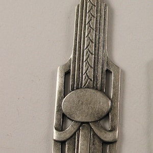 May include: A silver pendant with an Art Deco design. The pendant features a geometric pattern with a central oval shape.