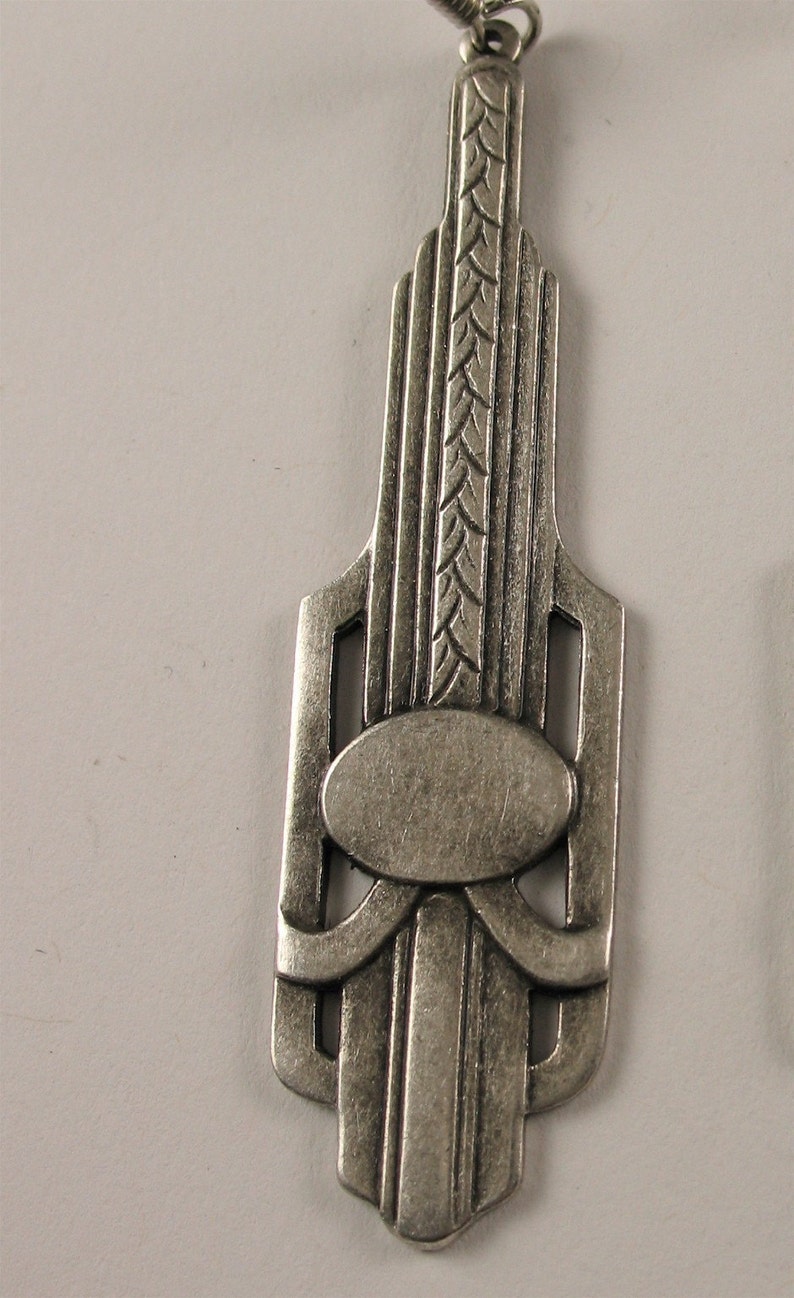 May include: A silver pendant with an Art Deco design. The pendant features a geometric pattern with a central oval shape.