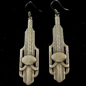May include: A pair of silver-toned dangle earrings with an Art Deco design. The earrings feature a geometric pattern with a central oval shape.