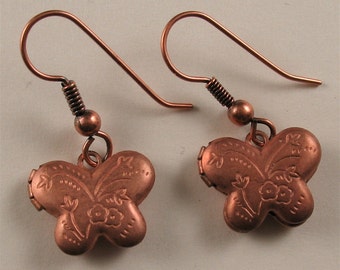 May include: A pair of copper butterfly earrings with a floral design. The earrings have a hook closure.