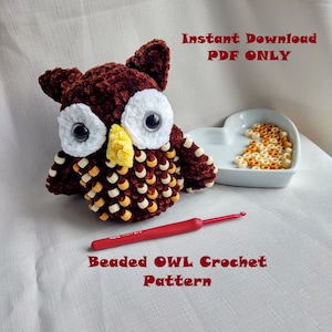 May include: A brown crocheted owl with white and yellow beads. The owl is sitting on a white surface with a heart-shaped dish of beads. The text "Instant Download PDF ONLY" and "Beaded OWL Crochet Pattern" is visible in the image.