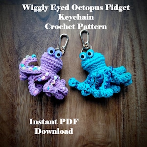 May include: Two crocheted octopus keychains, one purple and one turquoise, with wiggly eyes. The keychains are attached to silver clasps. Text on the image reads "Wiggly Eyed Octopus Fidget Keychain Crochet Pattern" and "Instant PDF Download."