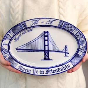 May include: Oval ceramic platter with a blue and white design. The platter features a detailed illustration of the Golden Gate Bridge, the date August 16th, 2025, and the words "Warm Ye in Friendship". The border has a decorative pattern.