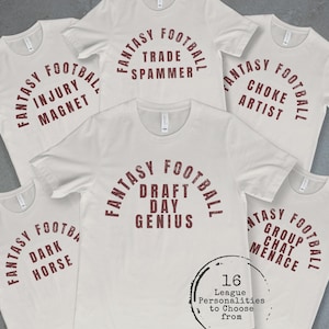 May include: A collection of light-colored t-shirts featuring dark red text. Each shirt displays the words Fantasy Football in an arch above specific phrases including Injury Magnet, Trade Spammer, Choke Artist, Draft Day Genius, Dark Horse, and Group Chat Menace. A circular graphic in the corner states 16 League Personalities to Choose from.