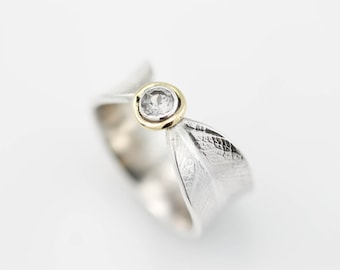 May include: A silver ring with a textured leaf design and a small round diamond set in a gold bezel.