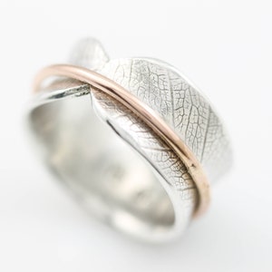 May include: A silver ring with a leaf design and a thin band of rose gold.