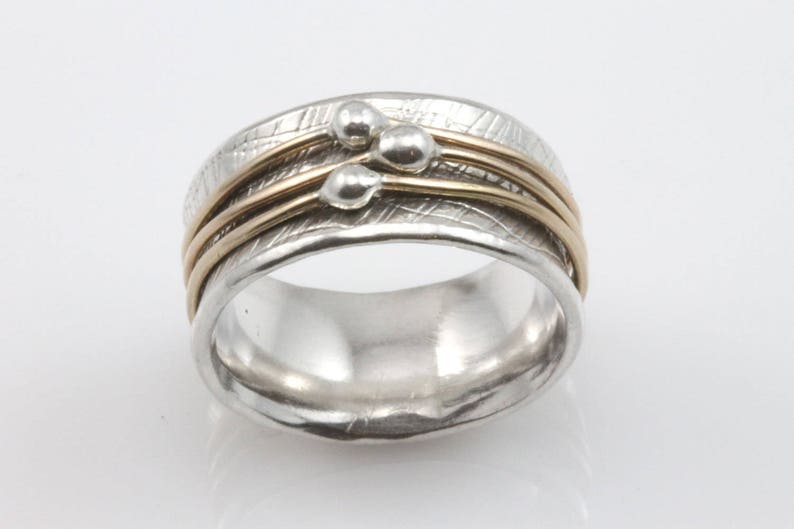 May include: A silver ring with three gold bands and a cluster of silver beads.
