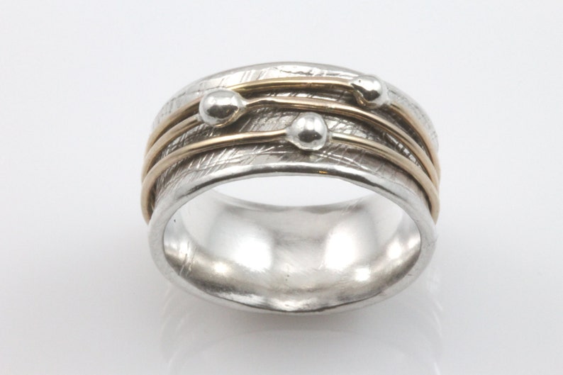 May include: A silver ring with three gold bands and three silver beads. The ring has a textured surface.