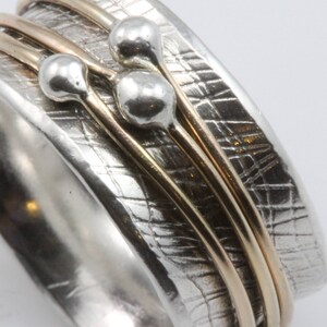 May include: A silver ring with a textured surface and three gold bands. The ring has three silver spheres attached to the bands.