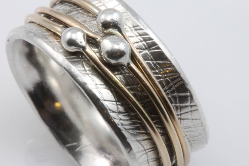 May include: A silver ring with a textured surface and three gold bands. The ring has three silver spheres attached to the bands.
