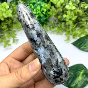 May include: A smooth, polished, grey and blue labradorite crystal wand with a pointed tip. The crystal has a unique iridescent sheen.
