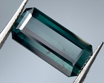 Può includere: Una pietra preziosa verde scuro con taglio rettangolare e finitura sfaccettata. La pietra preziosa è tenuta in posizione da una pinzetta.