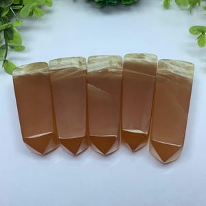 May include: Five orange and white carnelian crystal points, each with a pointed tip and a flat base. The points are arranged in a row, with the tips pointing to the right.