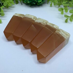 May include: Five orange and white calcite crystal points arranged in a row. The points are smooth and polished, with a slight translucence.