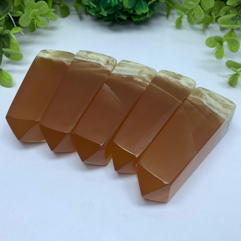 May include: Six orange and white agate crystal points, also known as carnelian, arranged in a row. The points are polished and have a smooth, glassy finish.