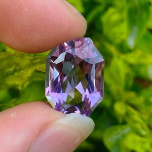 Peut inclure: Une pierre pr&eacute;cieuse d'am&eacute;thyste facet&eacute;e avec une teinte violette. La pierre pr&eacute;cieuse est taill&eacute;e en forme rectangulaire avec des bords biseaut&eacute;s.