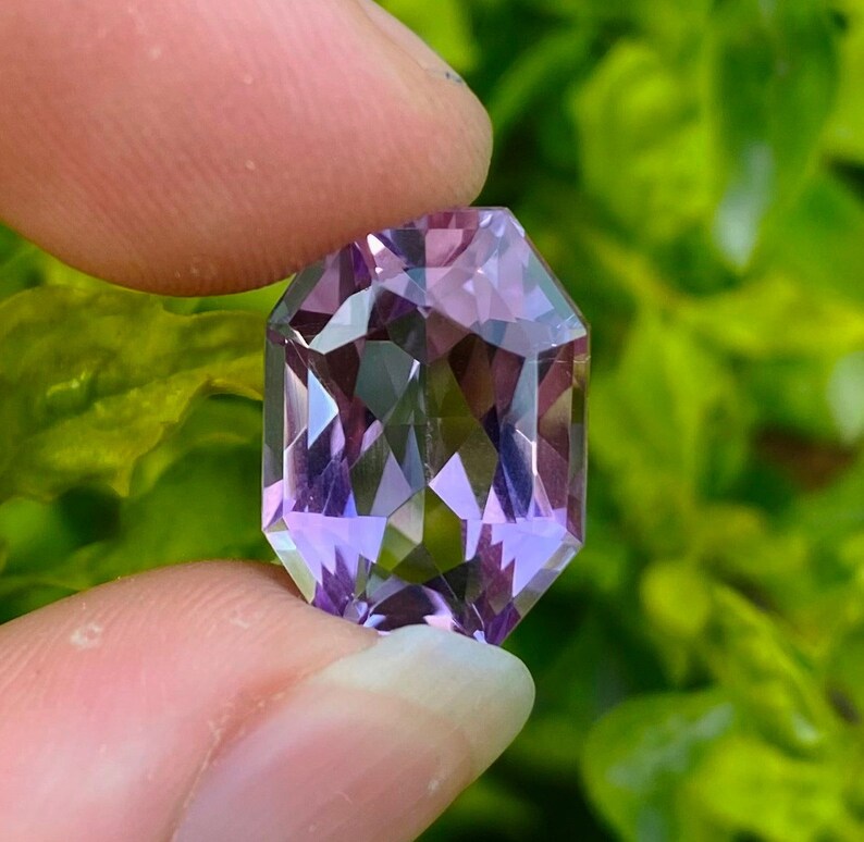 Peut inclure: Une pierre pr&eacute;cieuse d'am&eacute;thyste facet&eacute;e avec une teinte violette. La pierre pr&eacute;cieuse est taill&eacute;e en forme rectangulaire avec des bords biseaut&eacute;s.