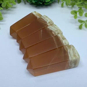 May include: Five orange and white calcite crystal points arranged in a fan shape. The points are polished and have a smooth, glassy finish.