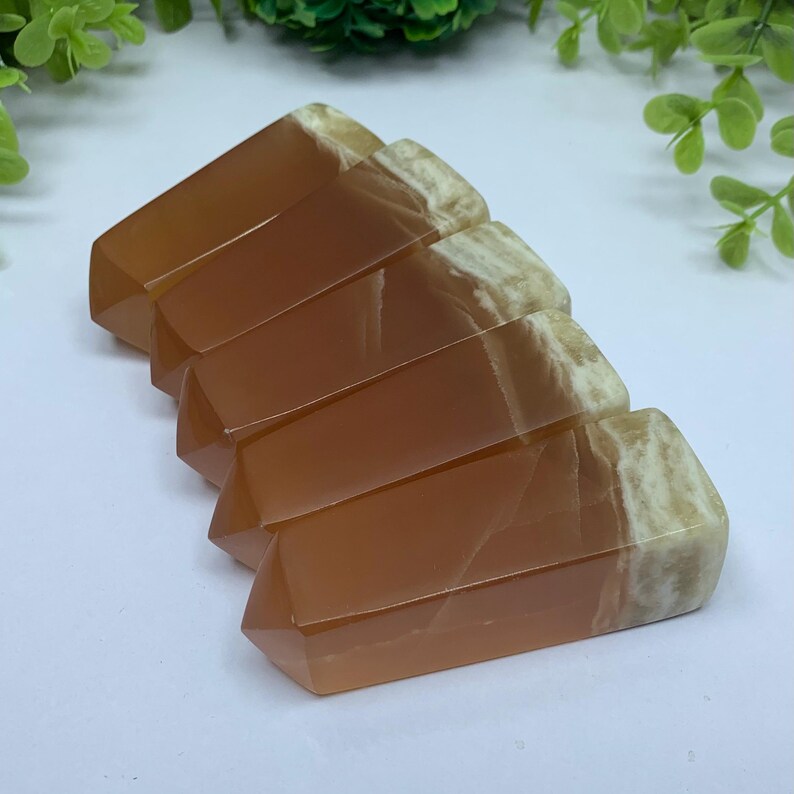 May include: Five orange and white calcite crystal points arranged in a fan shape. The points are polished and have a smooth, glassy finish.