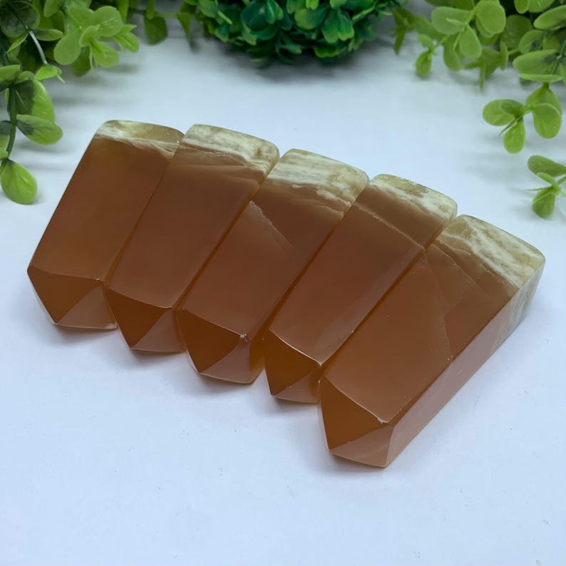 May include: Six brown and white agate crystal points, also known as carnelian, arranged in a row. The points are polished and have a smooth, glassy finish.