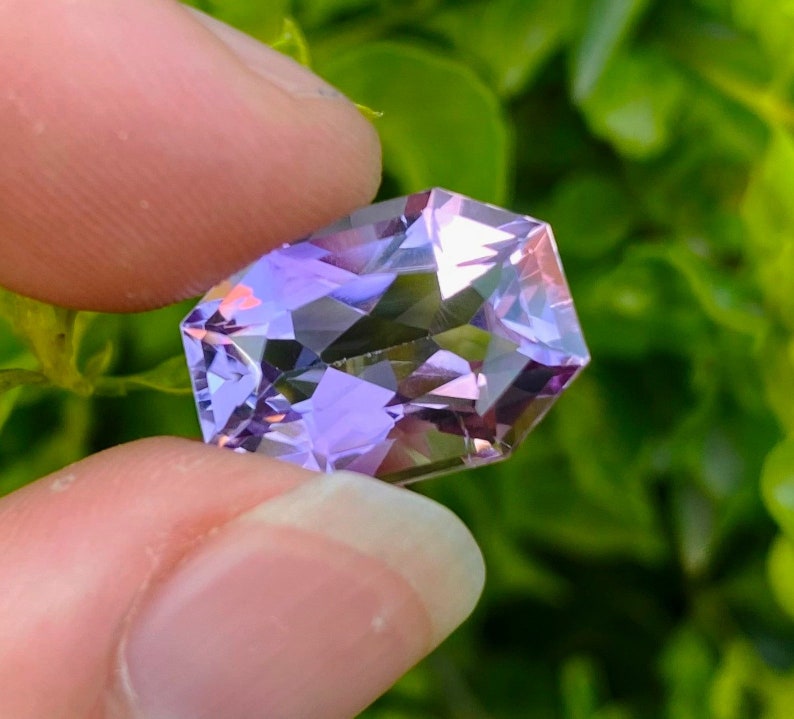 Peut inclure: Une pierre pr&eacute;cieuse d'am&eacute;thyste facet&eacute;e avec une teinte violette et rose. La pierre pr&eacute;cieuse est taill&eacute;e en forme octogonale et a un haut poli.