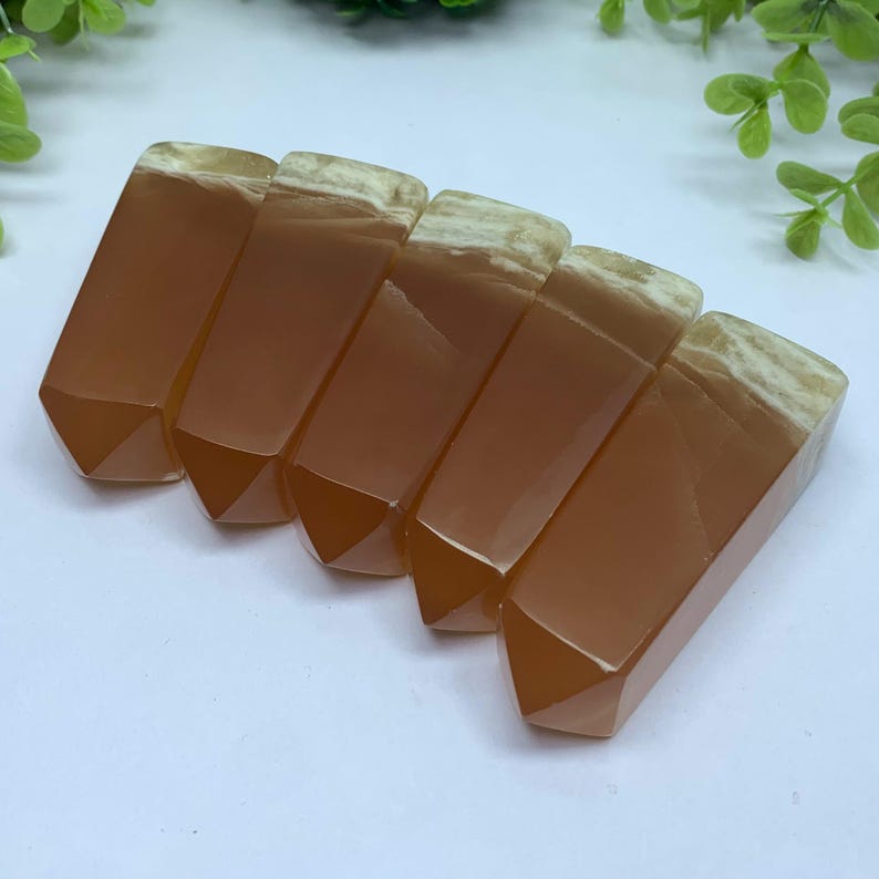 May include: Six orange and white carnelian crystal points arranged in a row. The points are all roughly the same size and shape, and they have a smooth, polished finish.