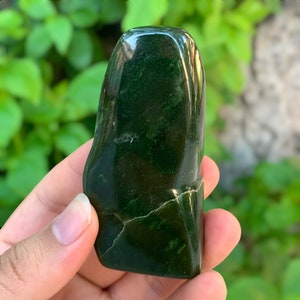 May include: A smooth, dark green jade stone with a natural, irregular shape. The stone has a polished finish and a subtle sheen.