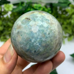 Puede incluir: Una esfera verde y blanca con un patrón de mármol. La esfera es lisa y pulida.