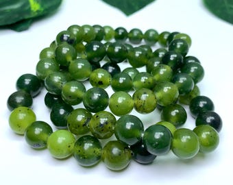 Pode incluir: Várias pulseiras de contas de jade verde. As contas esféricas exibem uma gama de tons verdes, algumas com manchas mais escuras. As pulseiras são dispostas artisticamente, destacando as variações naturais da pedra. Cada conta mede aproximadamente 1 cm de diâmetro.